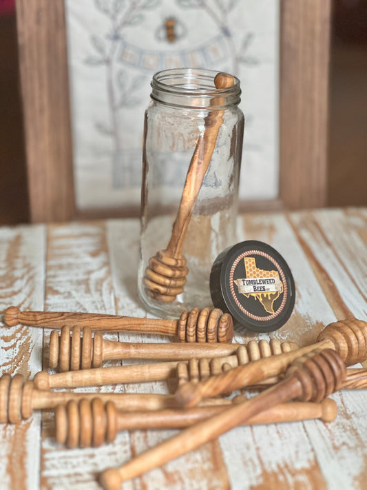 clear jar with wooden honey dipper inside, plus several honey dippers randomly laid out in front of the jar